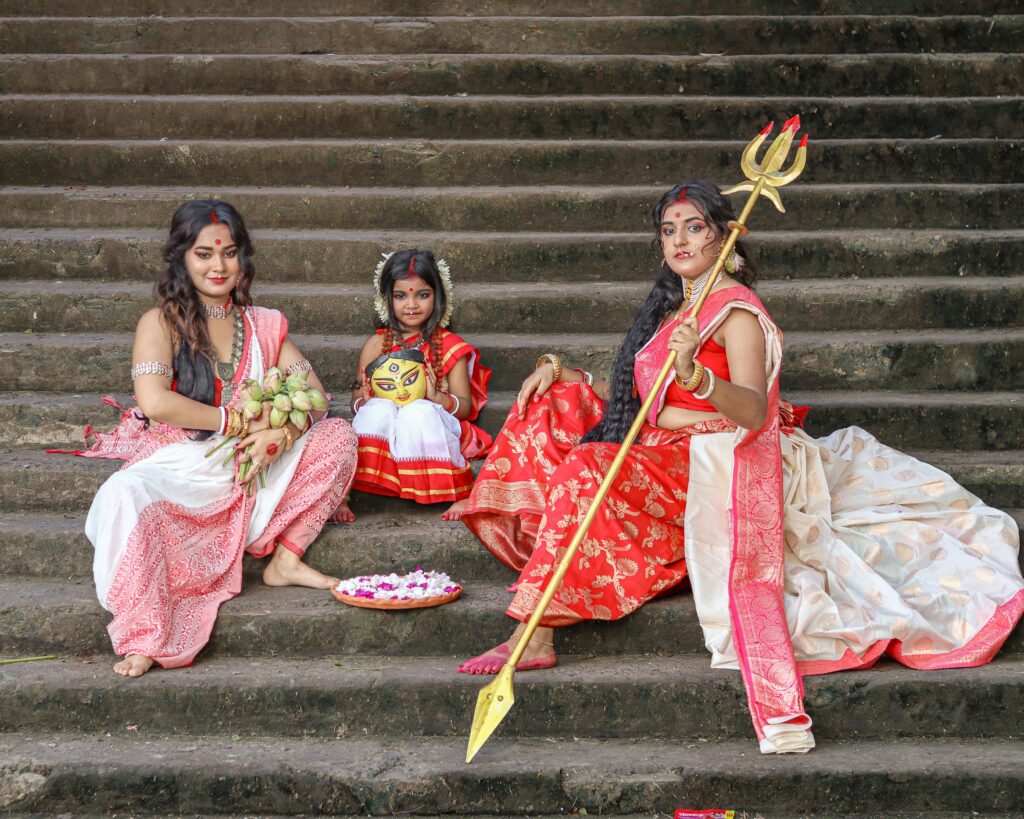 How to Identify the Authentic Garad Saree Three women in traditional Indian attire sit on stone steps with cultural items.
